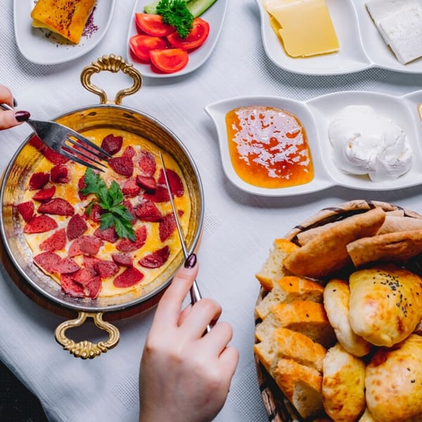 Mustard Cafe's breakfast spread with a person eating sausage and egg, bread, cheese, and jam.