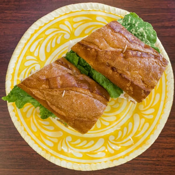 Two halves of a Mustard Cafe breakfast sandwich with lettuce on a yellow patterned plate.