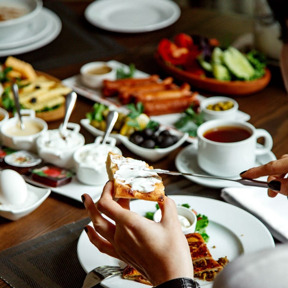 A person spreading cream cheese on a piece of toast at a table laden with breakfast dishes.